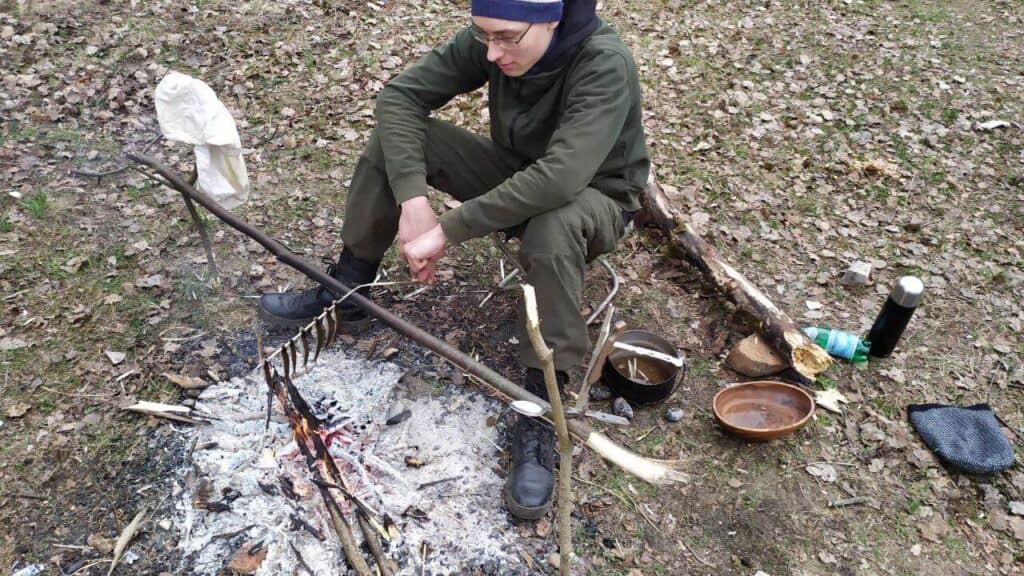 человек жарит рыбу уклейку на костре на палке
